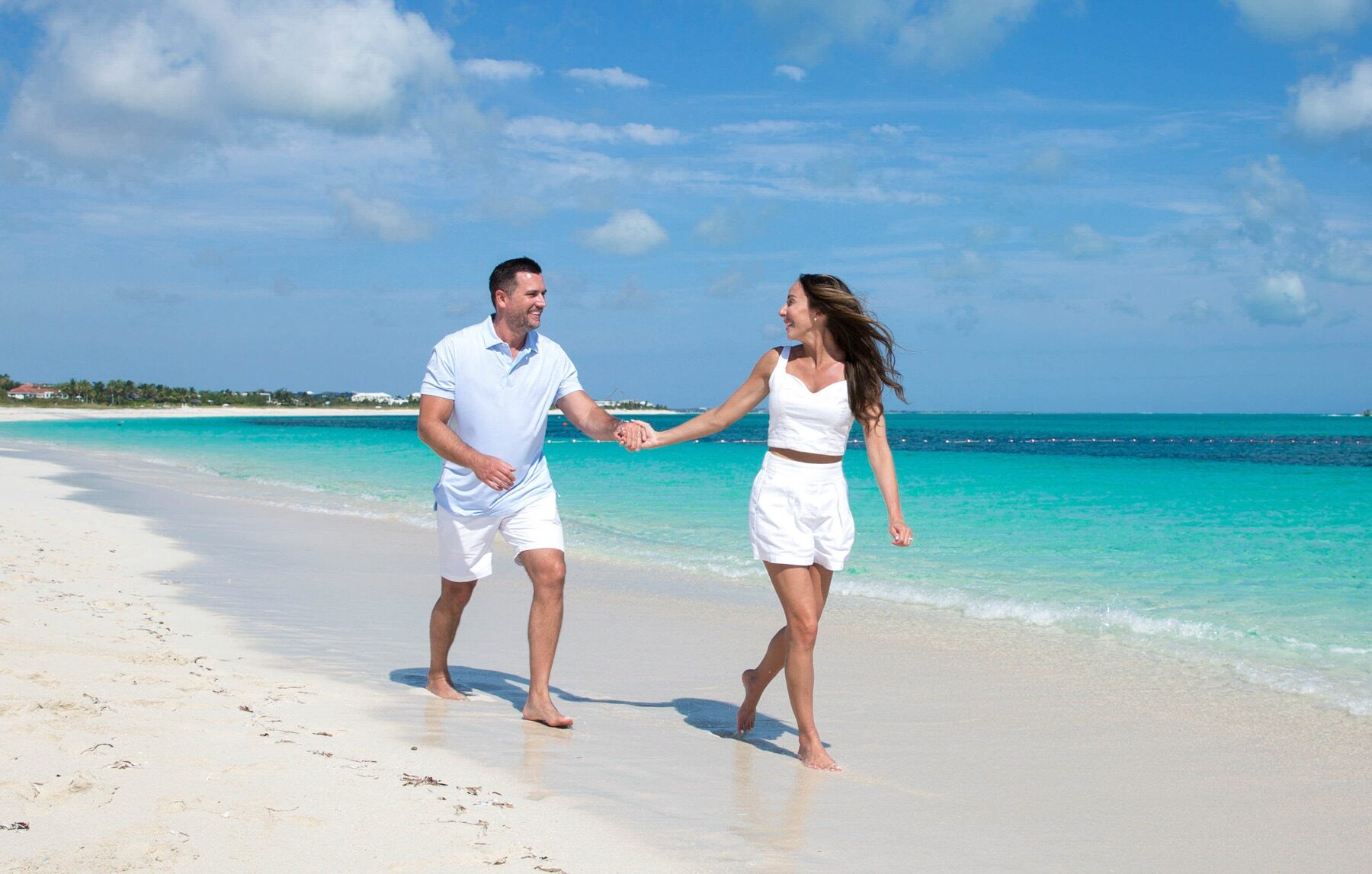 Couple in white running hand in hand along a bright sandbar