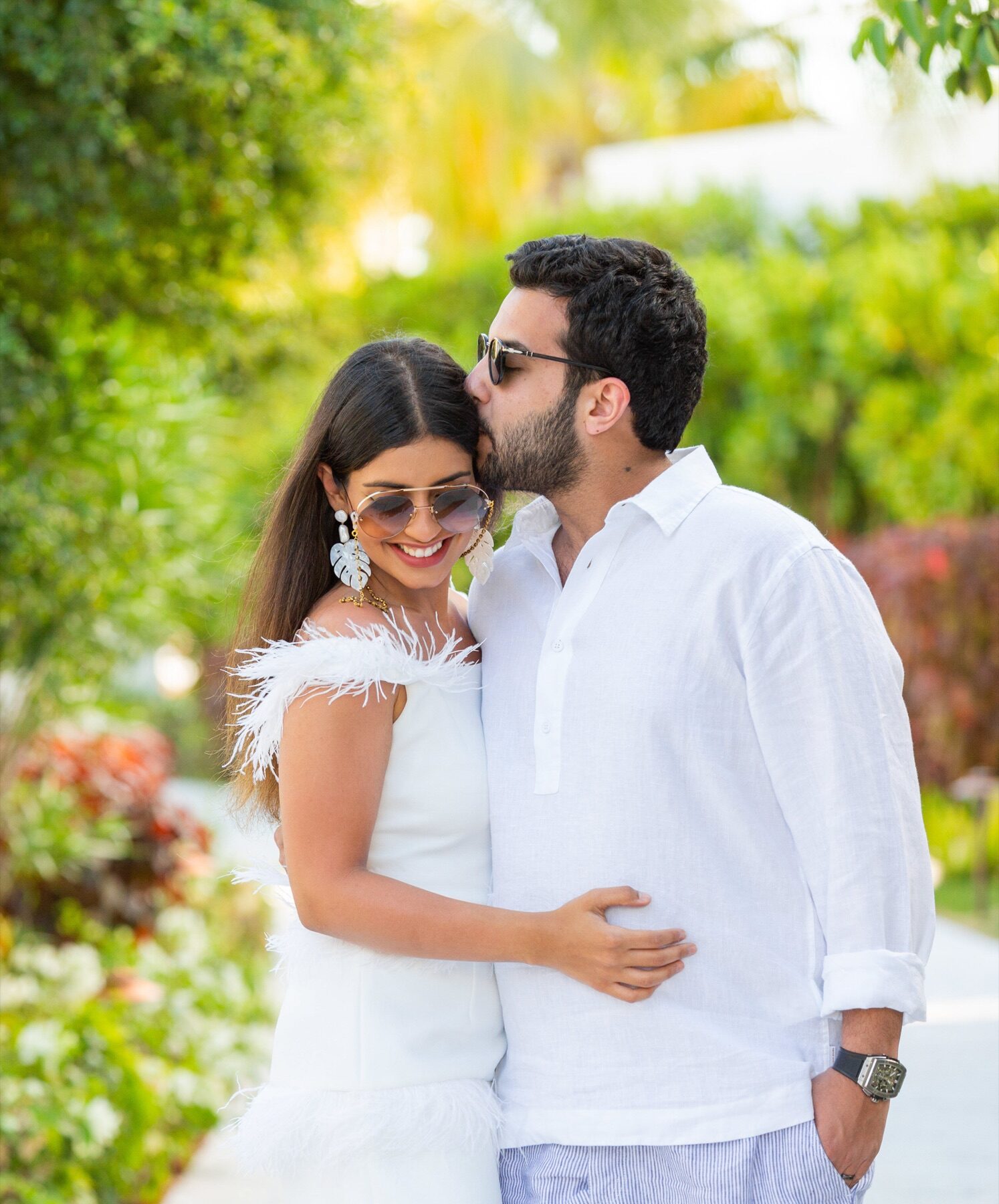 Man kissing his partner's forehead on a garden path lined with greenery