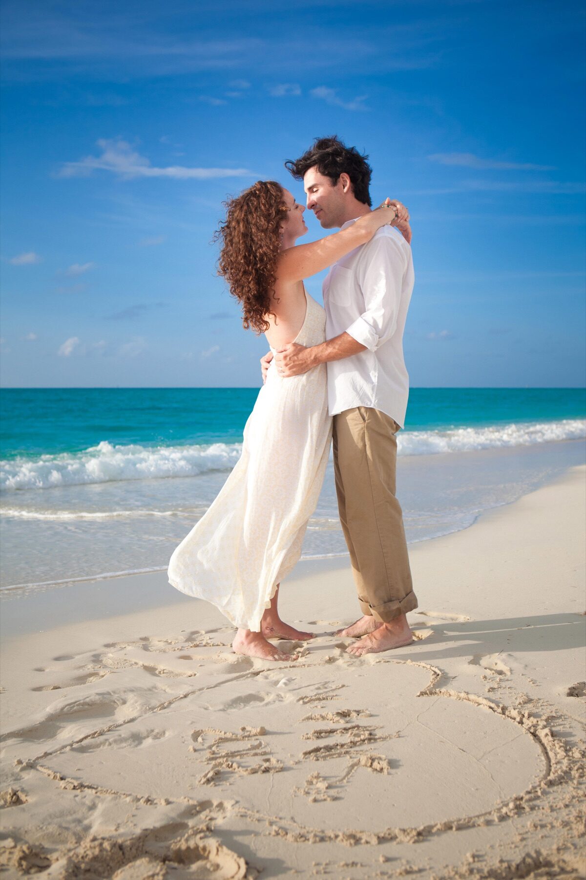 Couple embracing on the beach beside a heart drawn in the sand