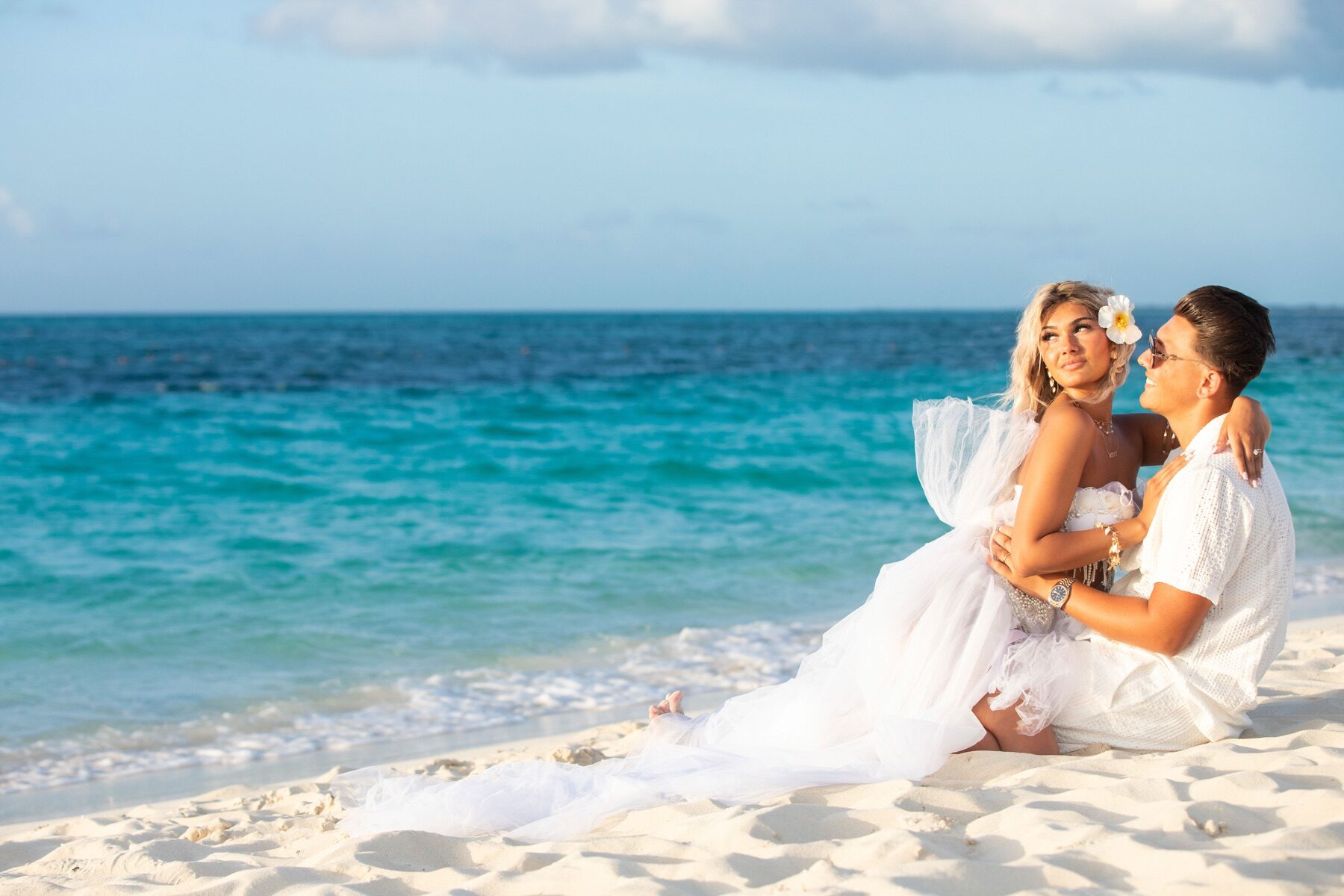 Couple sitting together on the sand at dusk, woman with a flower in her hair