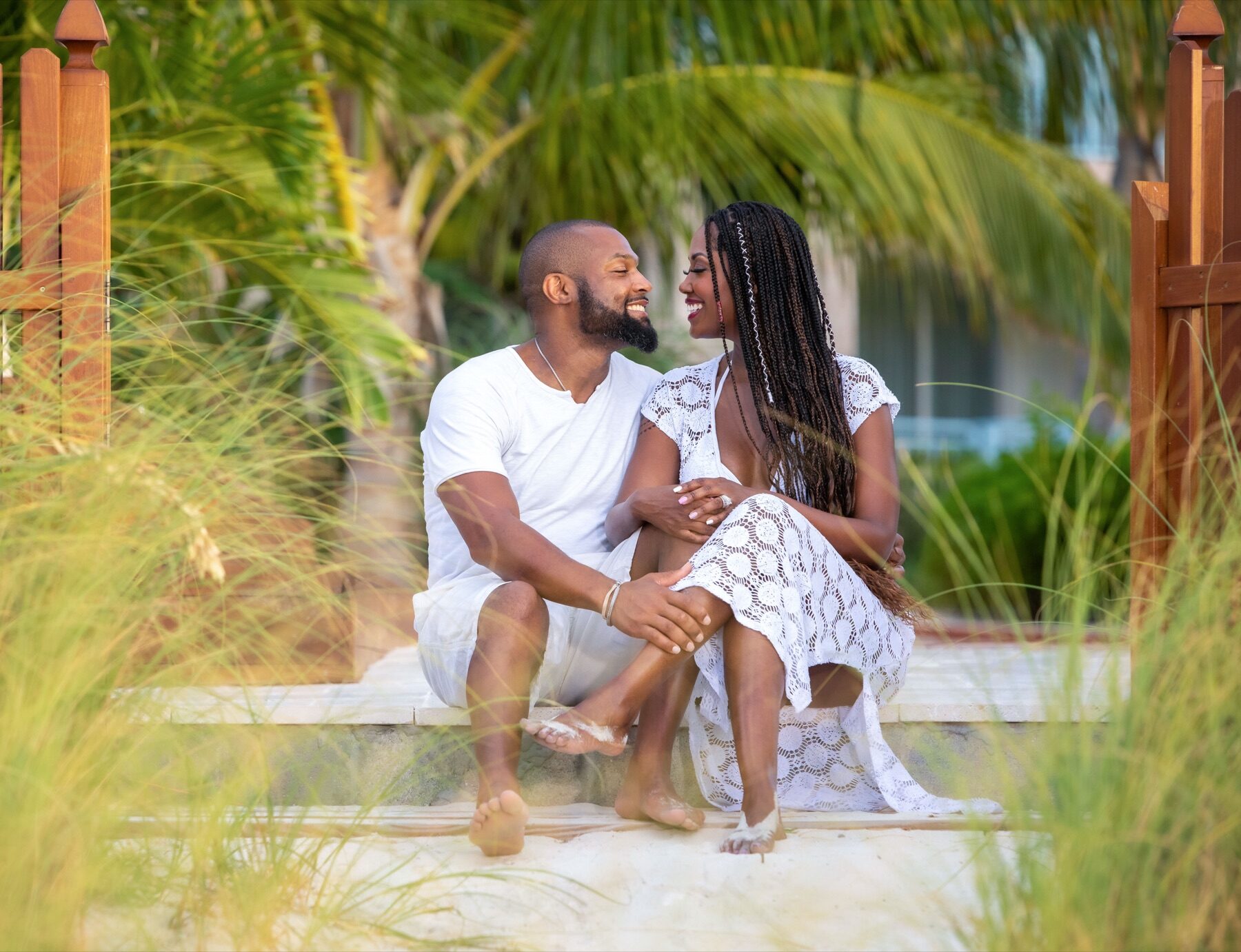 Couple laughing on a wooden dock in Turks and Caicos, framed by palm leaves