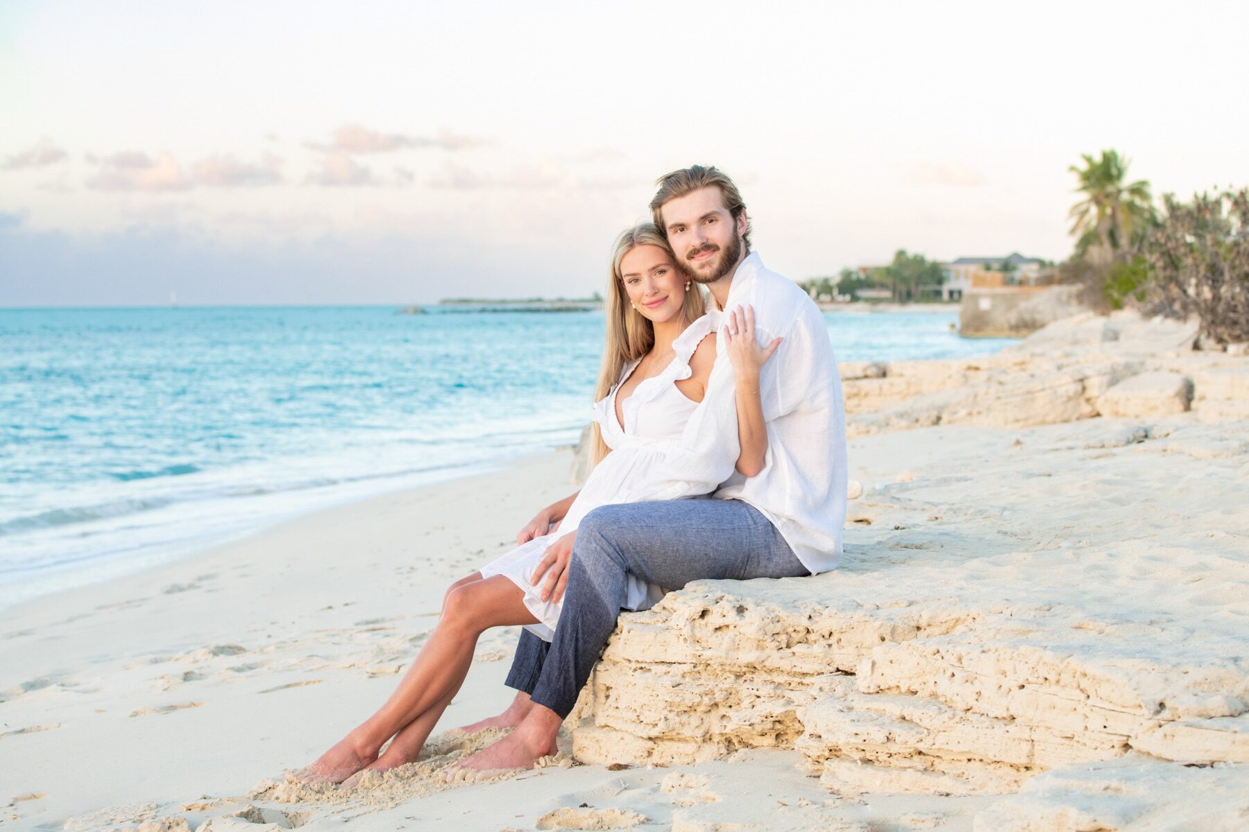 Couple sitting on a rock ledge in Turks and Caicos, smiling at the camera