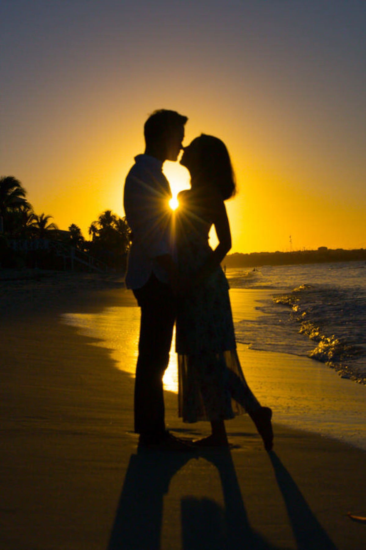 Silhouette of a couple kissing on the beach against a glowing orange sunset