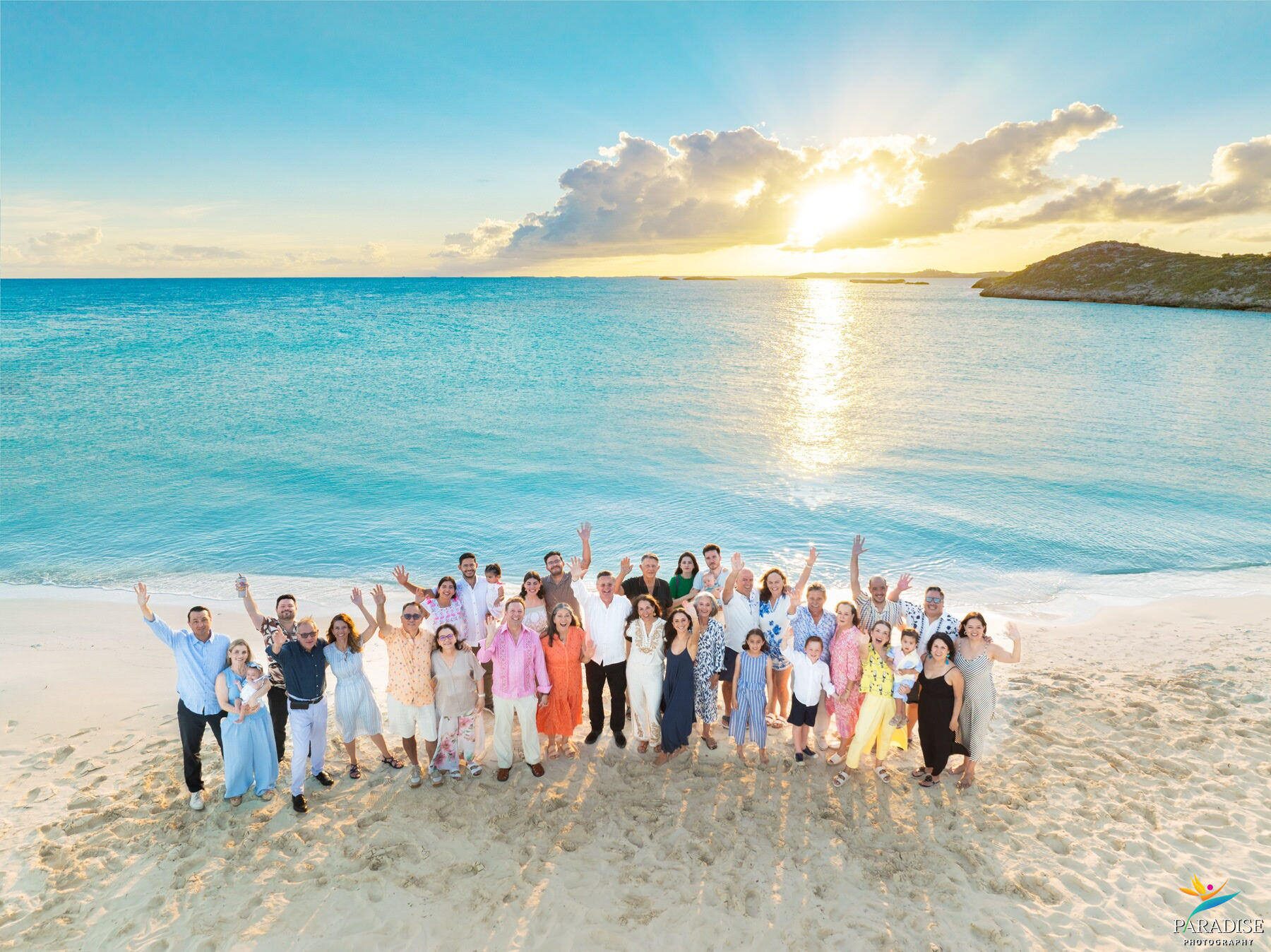 Large extended family cheering with arms raised on the beach at sunrise