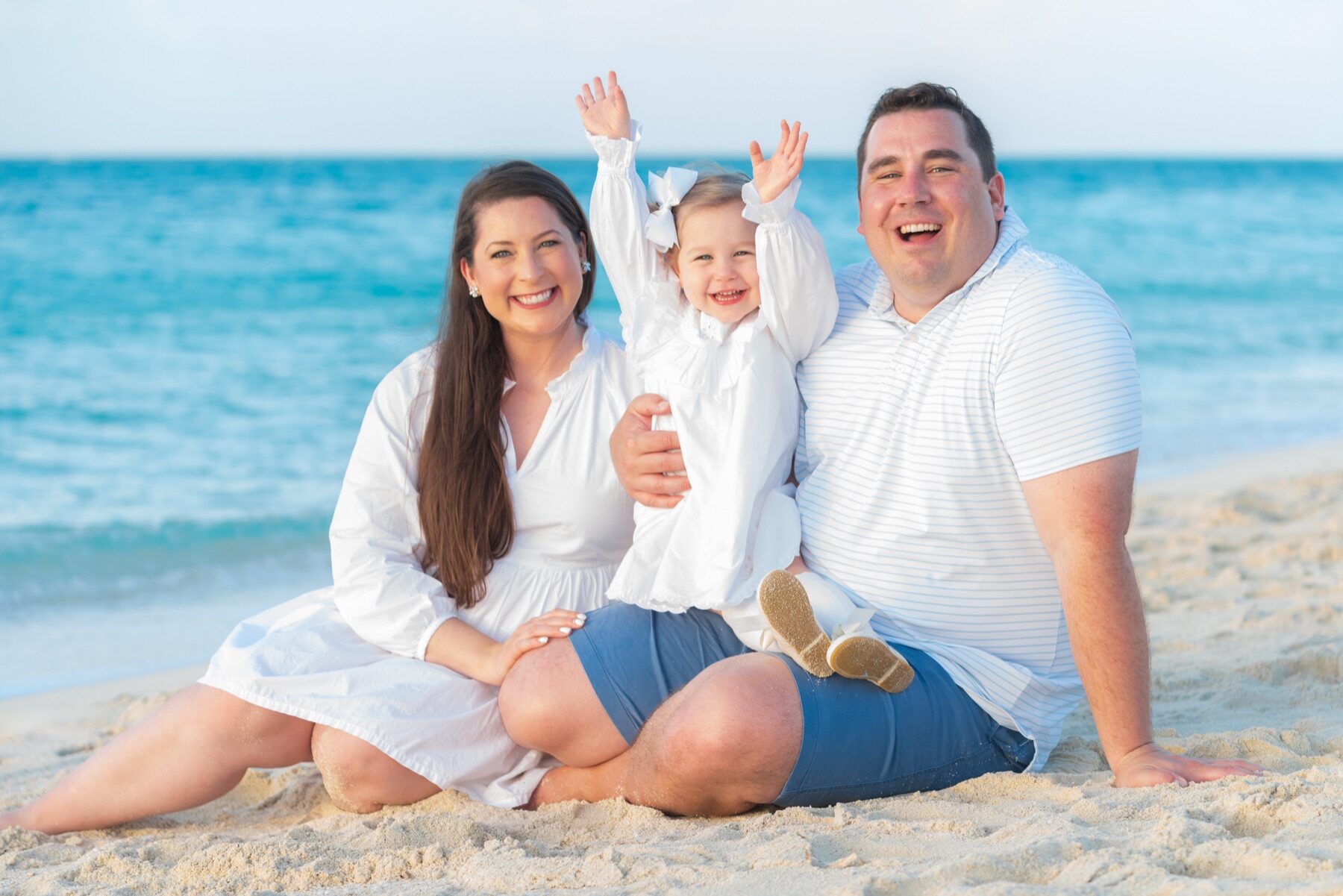Parents laughing with their toddler raising both arms on a Turks and Caicos beach