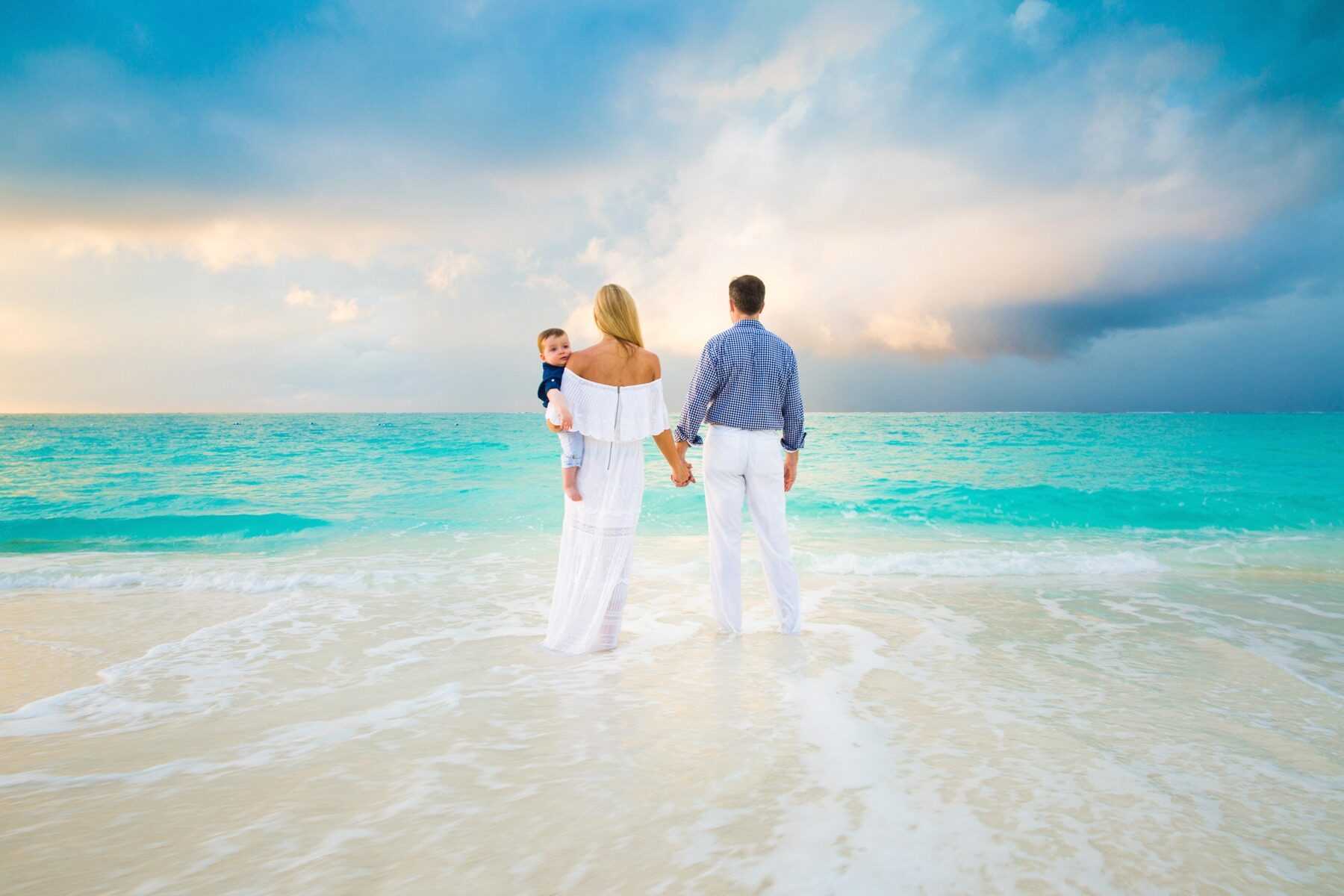 Family of three viewed from behind holding hands, facing the turquoise sea