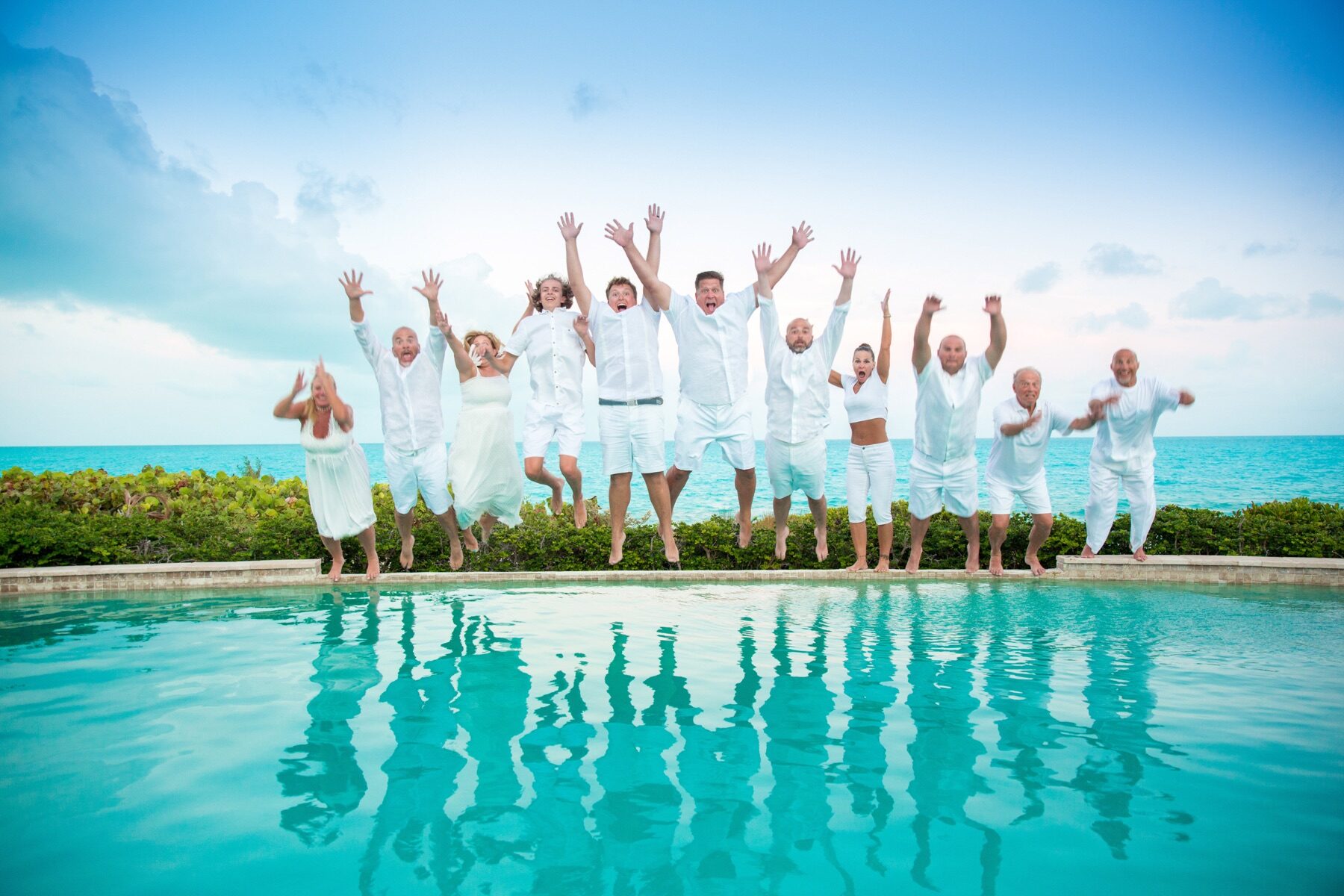 Large group jumping for joy poolside in Turks and Caicos, arms raised high