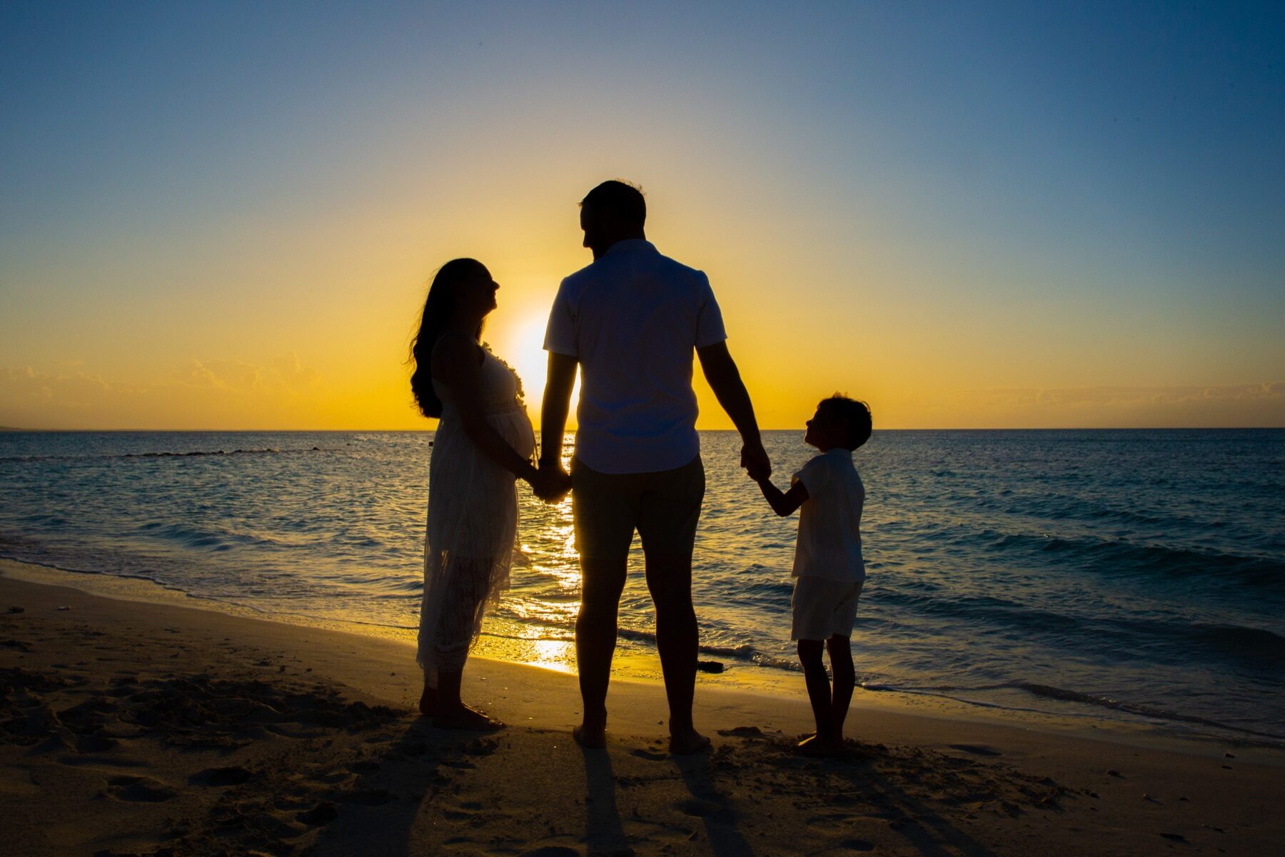 Silhouette of parents and young son holding hands facing the sunset