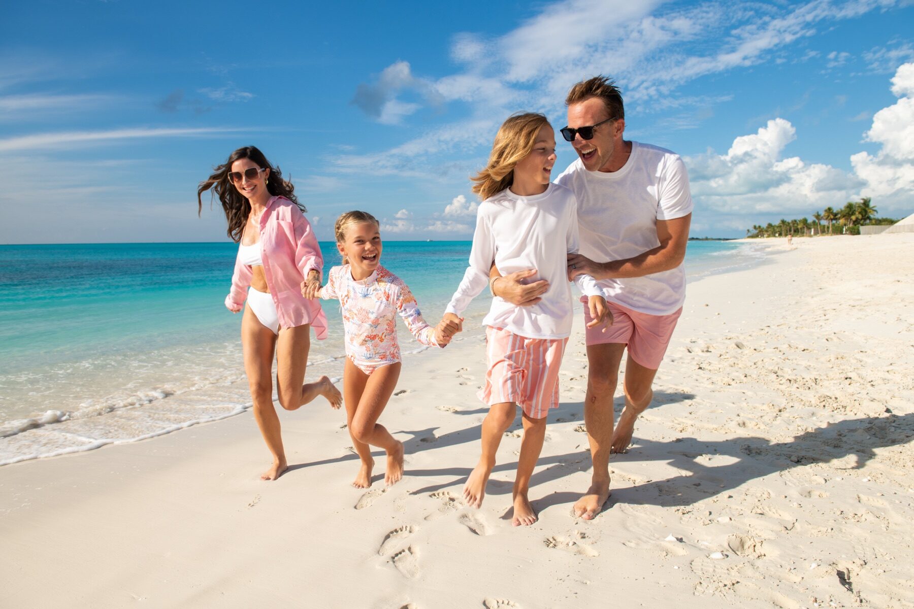 Family of four running barefoot along a white sand beach in Turks and Caicos