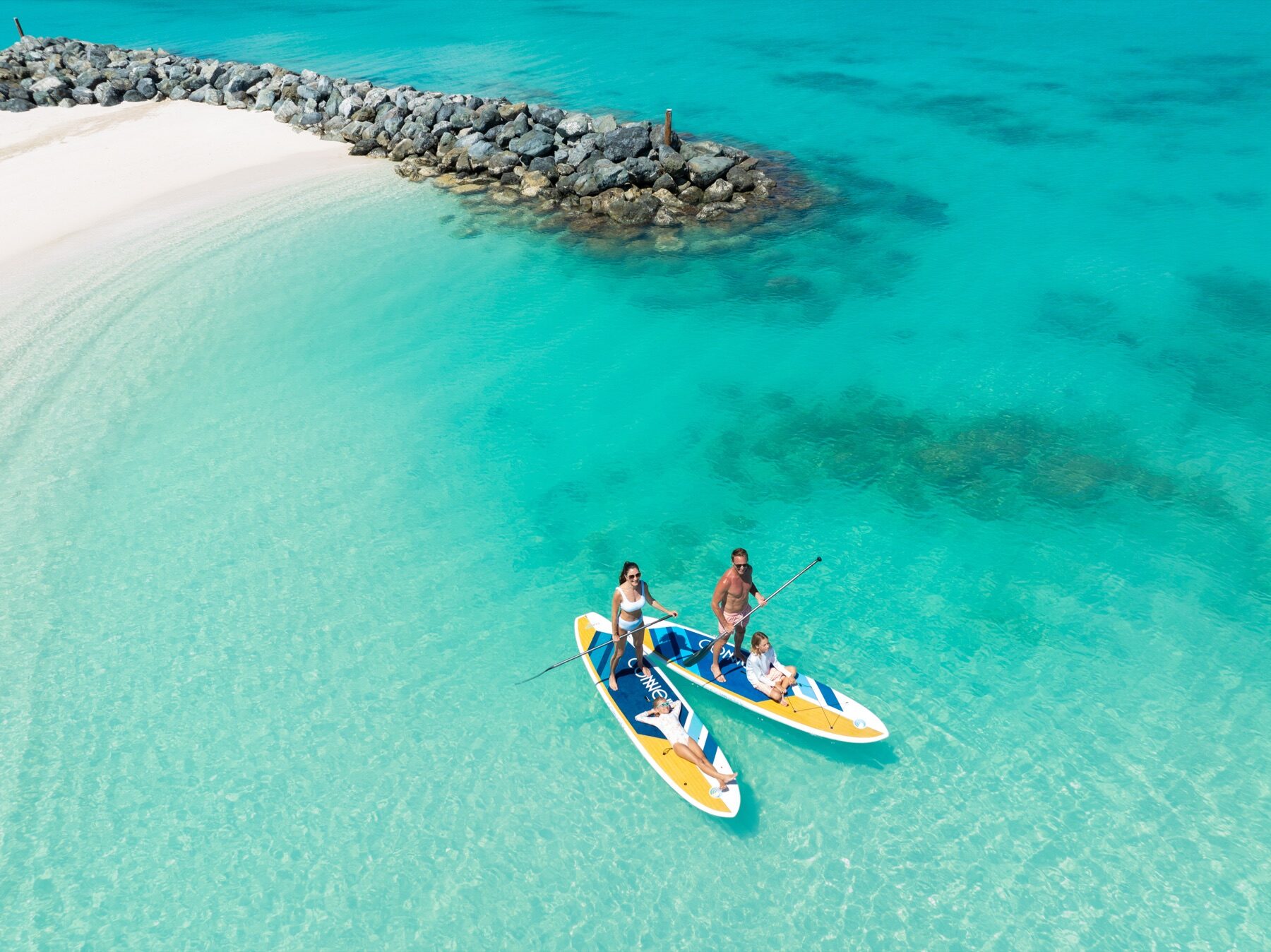 Aerial view of a family paddleboarding over clear shallow reef water