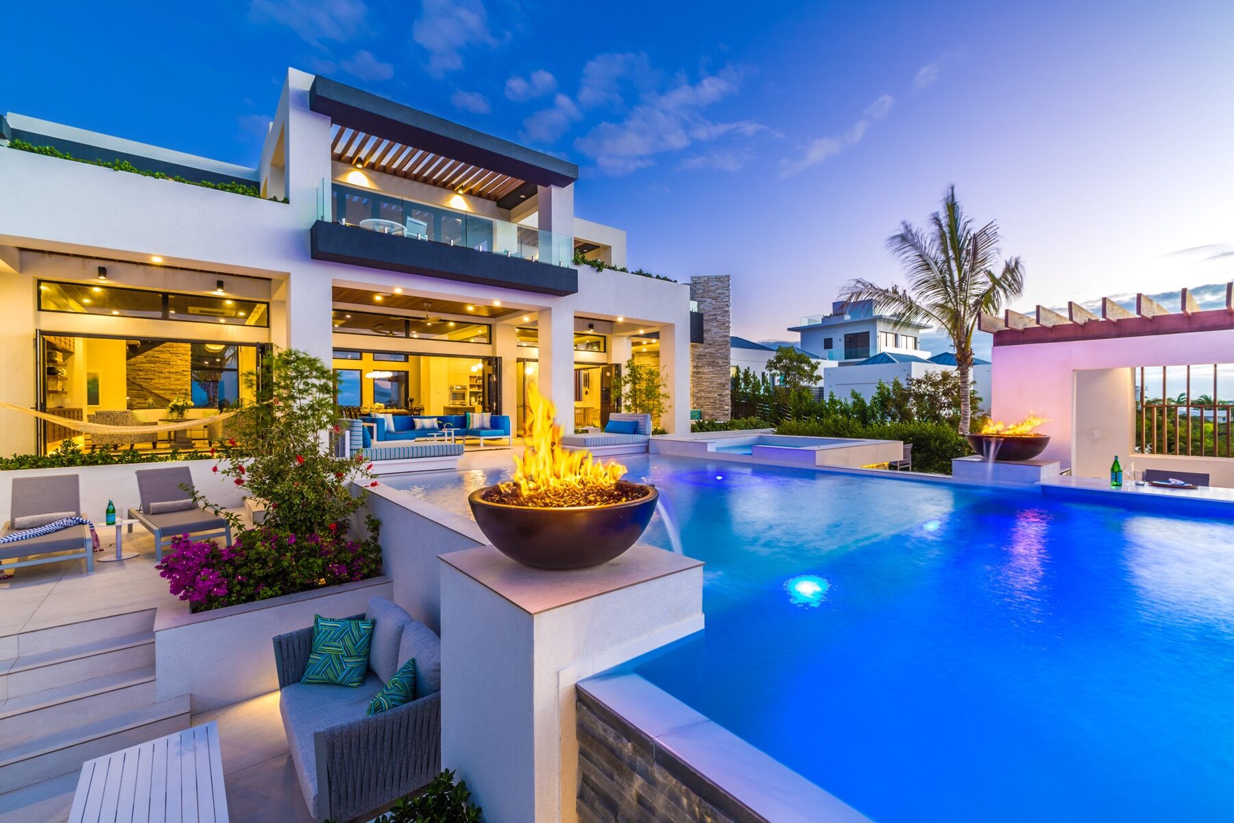 Modern villa exterior with fire bowls glowing beside an illuminated pool