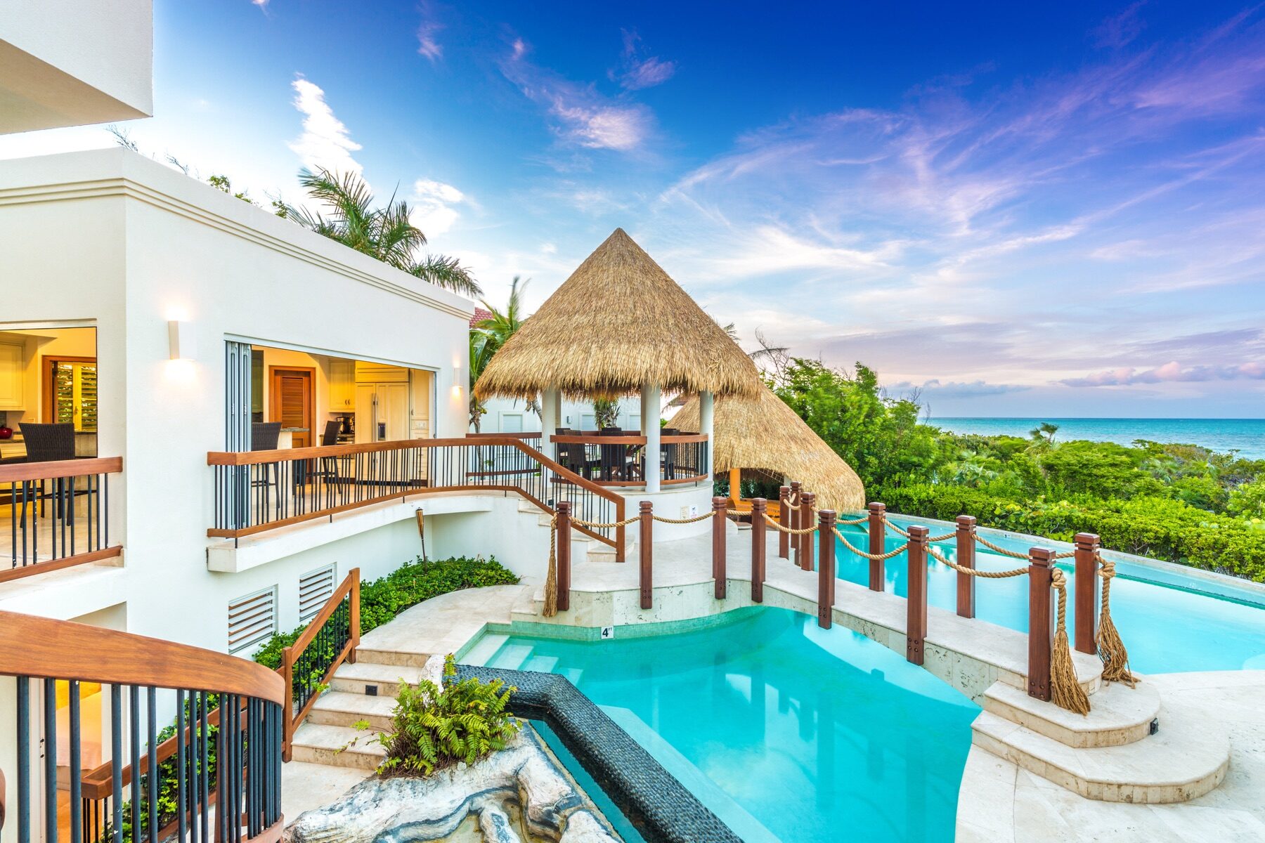 Thatched roof cabana connected by a wooden bridge over a resort pool