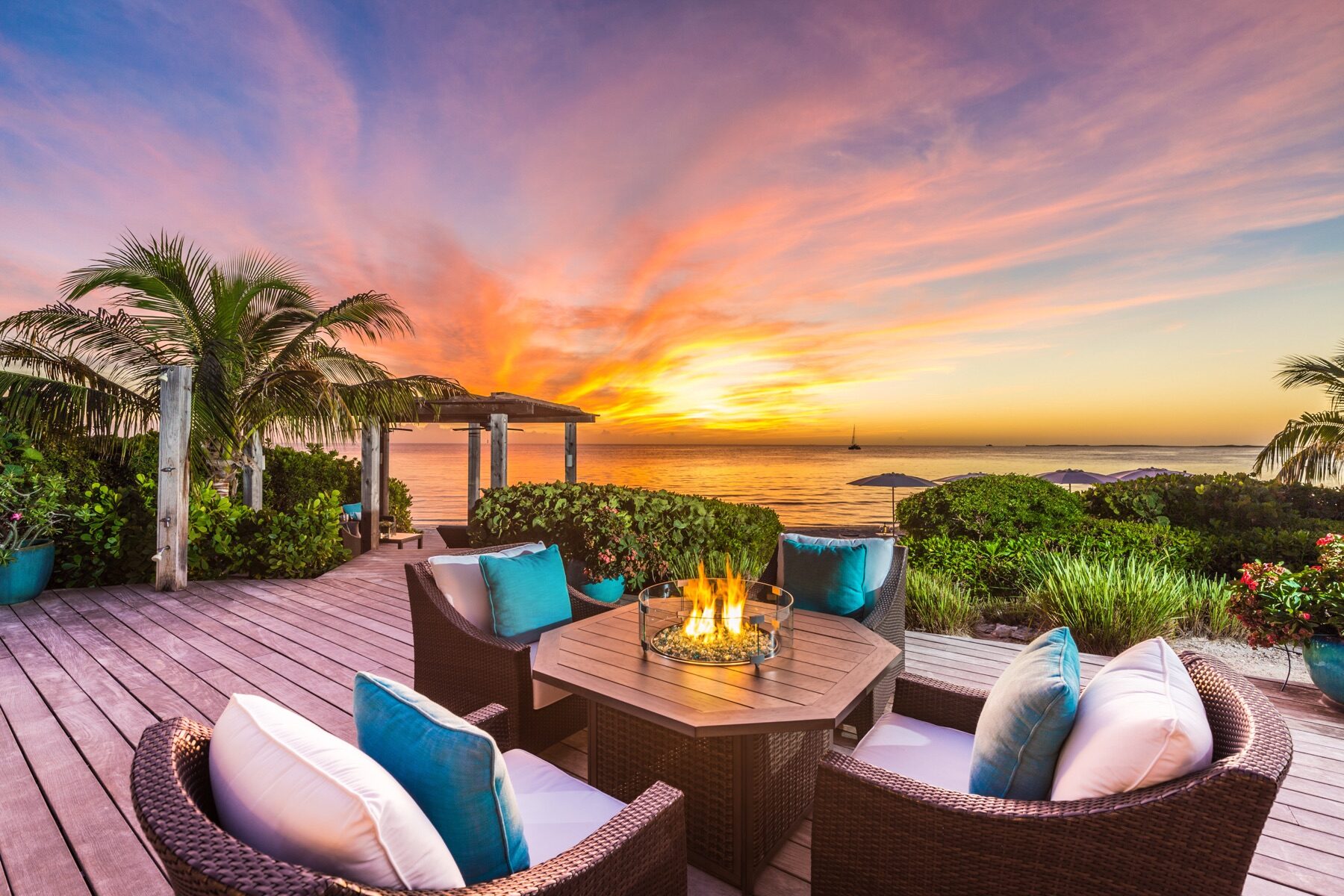 Beachfront patio seating arranged around a fire table at sunset