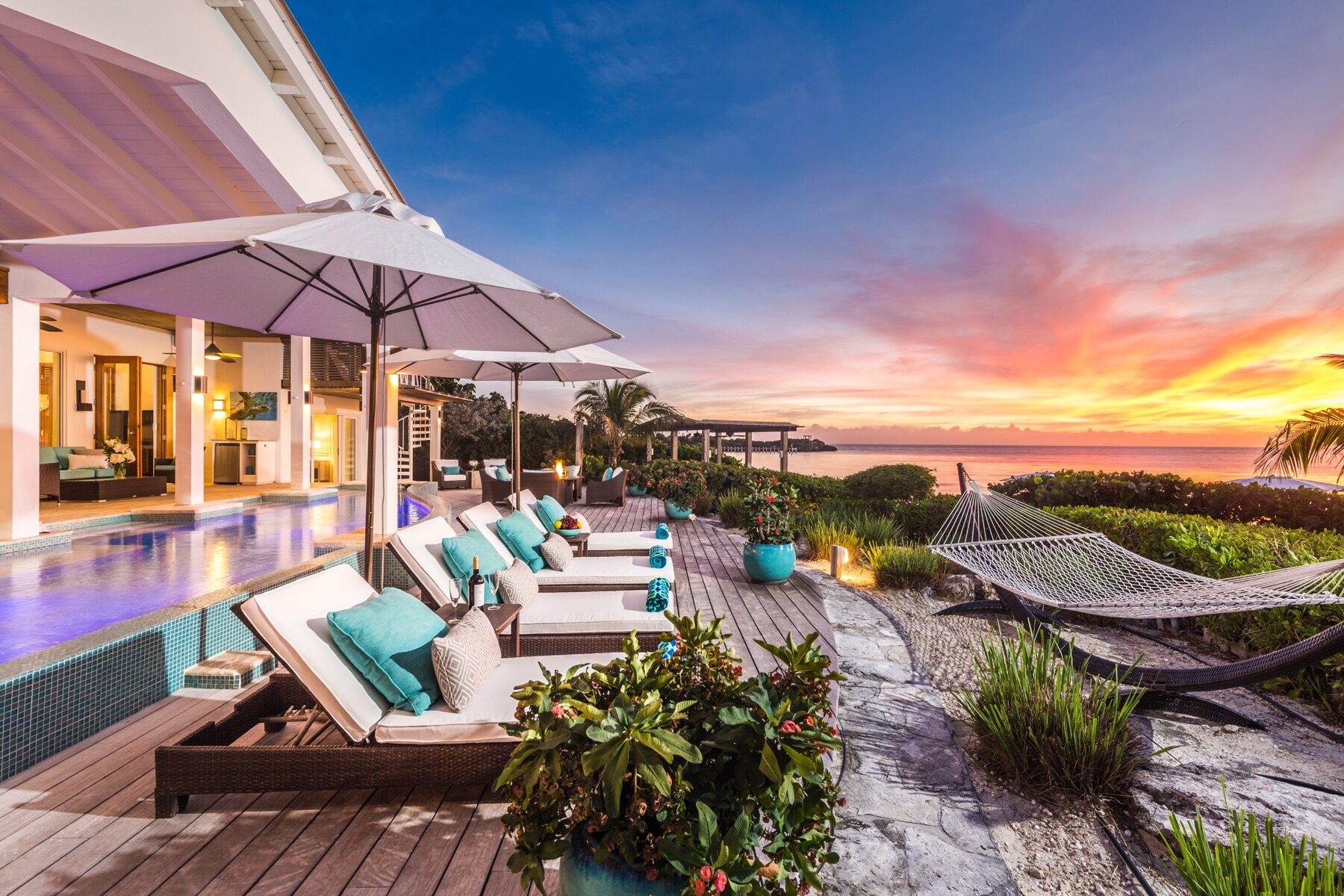 Sunset view along a villa pool deck lined with lounge chairs and umbrellas