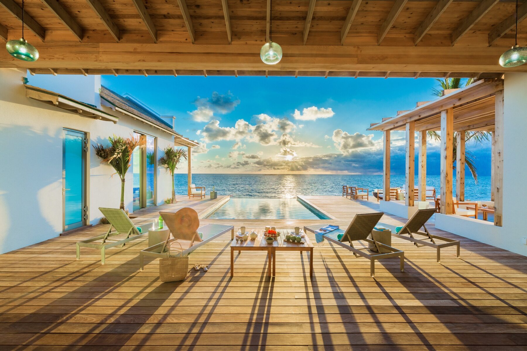 Covered wooden deck with lounge chairs facing an oceanfront infinity pool