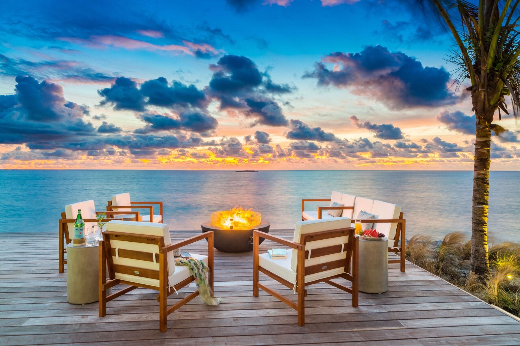 Fire pit surrounded by wooden chairs on a beachfront deck at dusk
