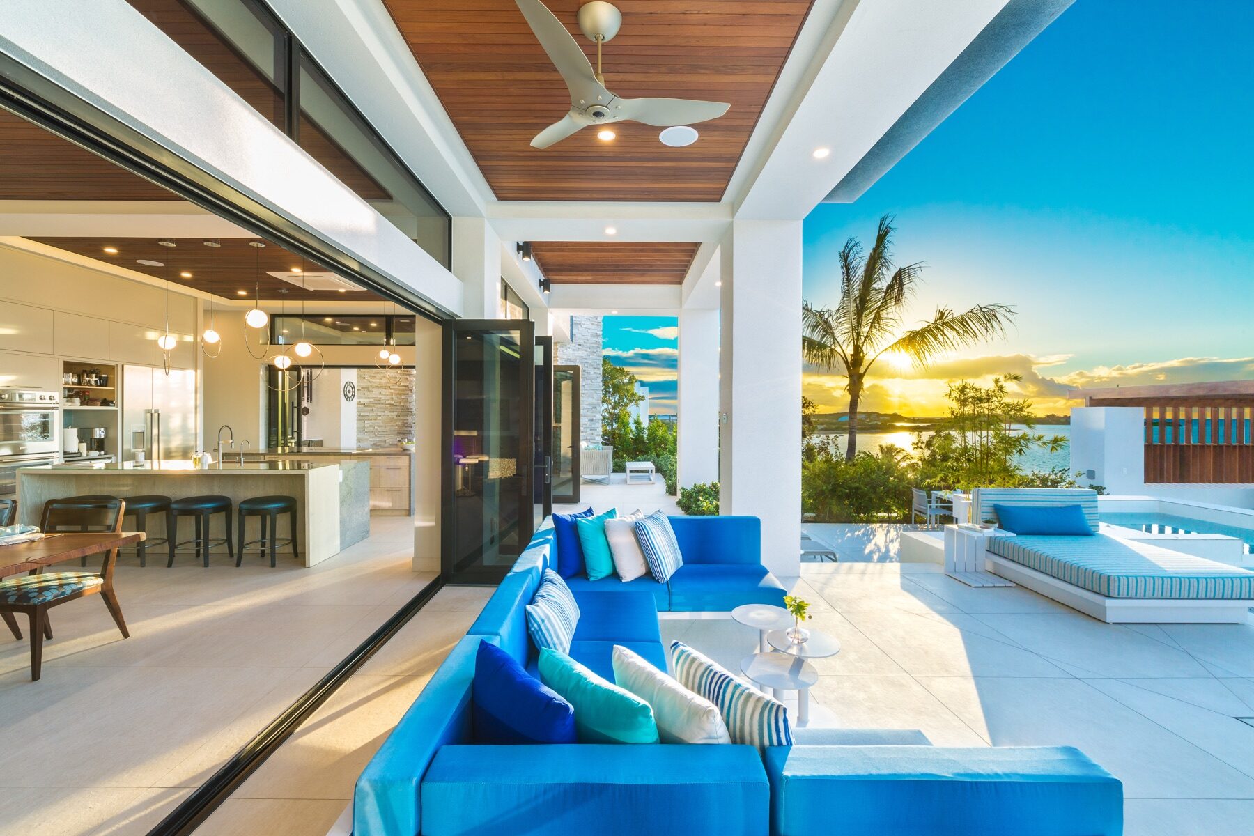 Open kitchen and blue sofa lounge overlooking a pool at sunset