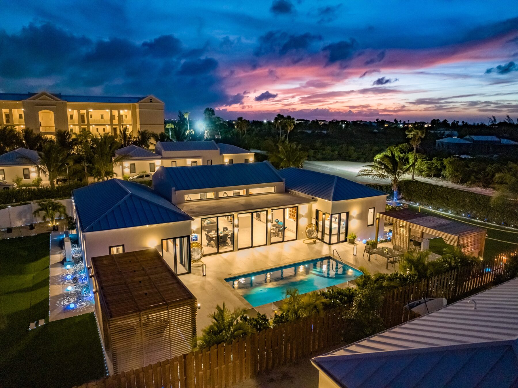 Aerial dusk view of a villa with a lit pool and wooden pergola