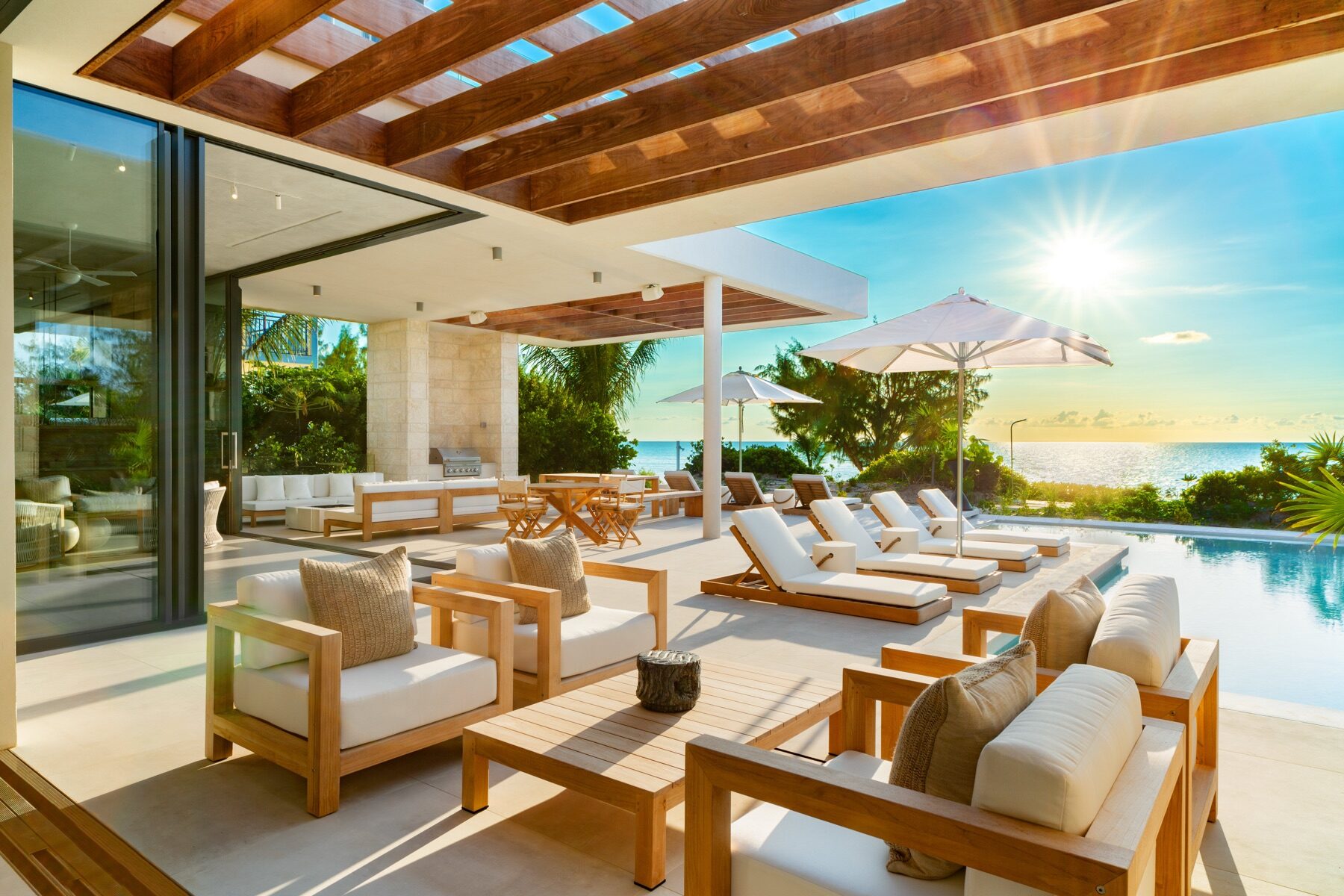 Covered patio with wooden lounge chairs facing the ocean at sunrise