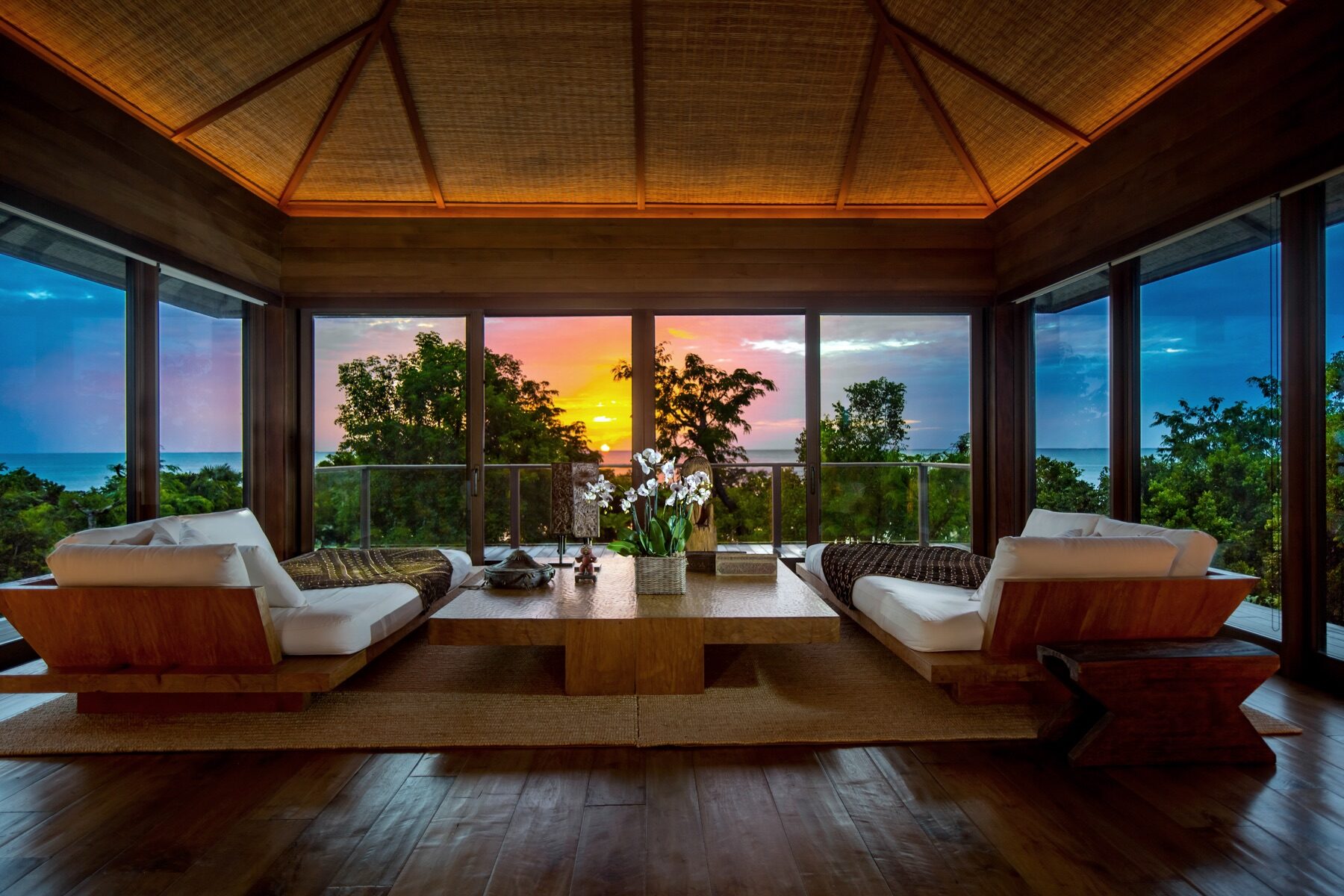 Thatched roof living room with two daybeds facing a colorful sunset