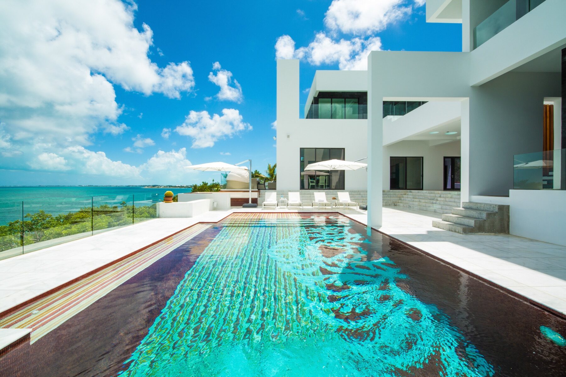 Long tiled infinity pool beside a white modern villa under blue sky