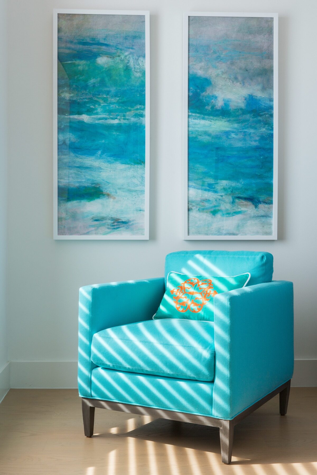 Turquoise accent chair with monogrammed pillow beneath framed ocean art