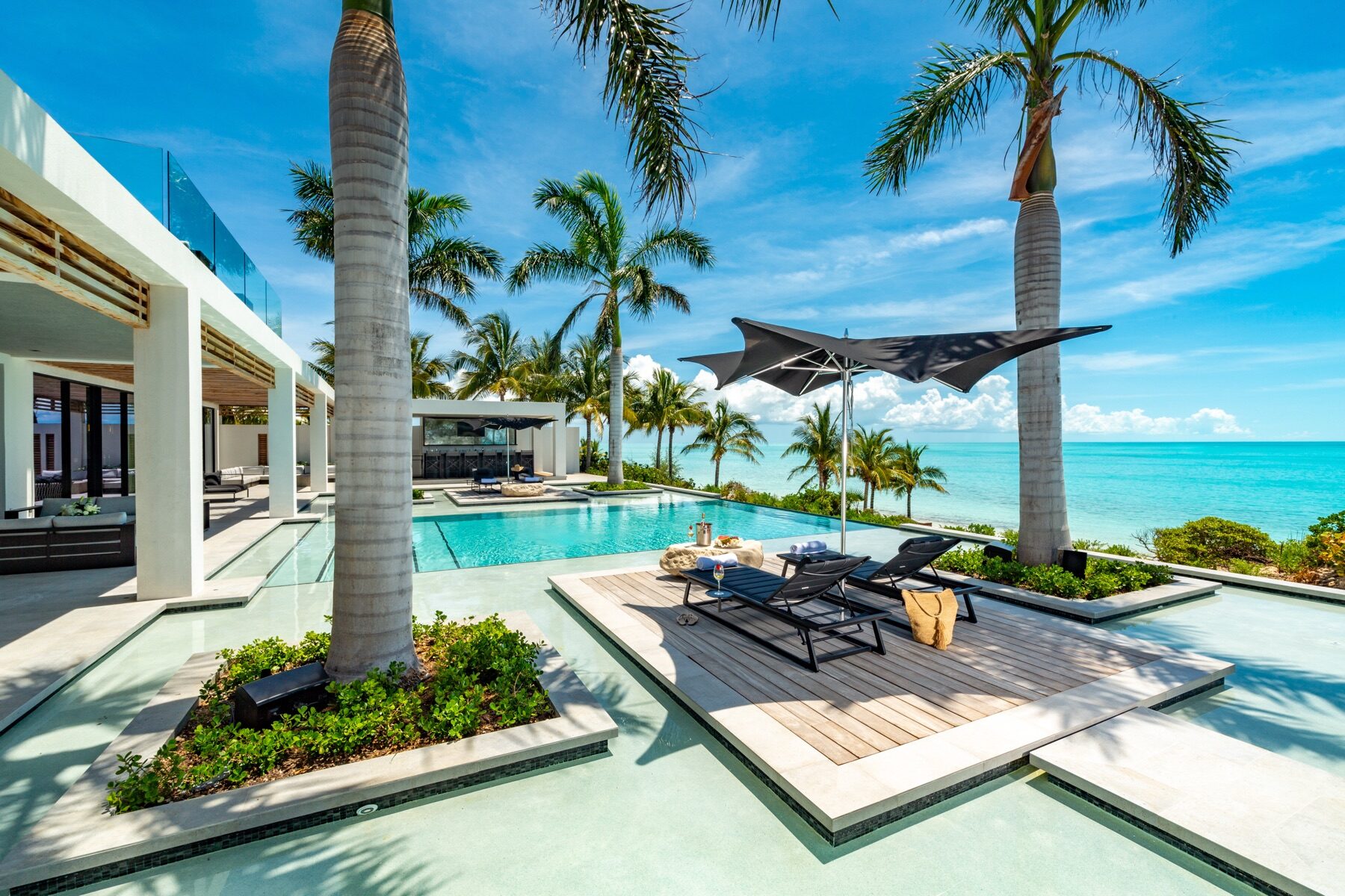 Poolside daybed shaded by palm trees with an ocean view beyond