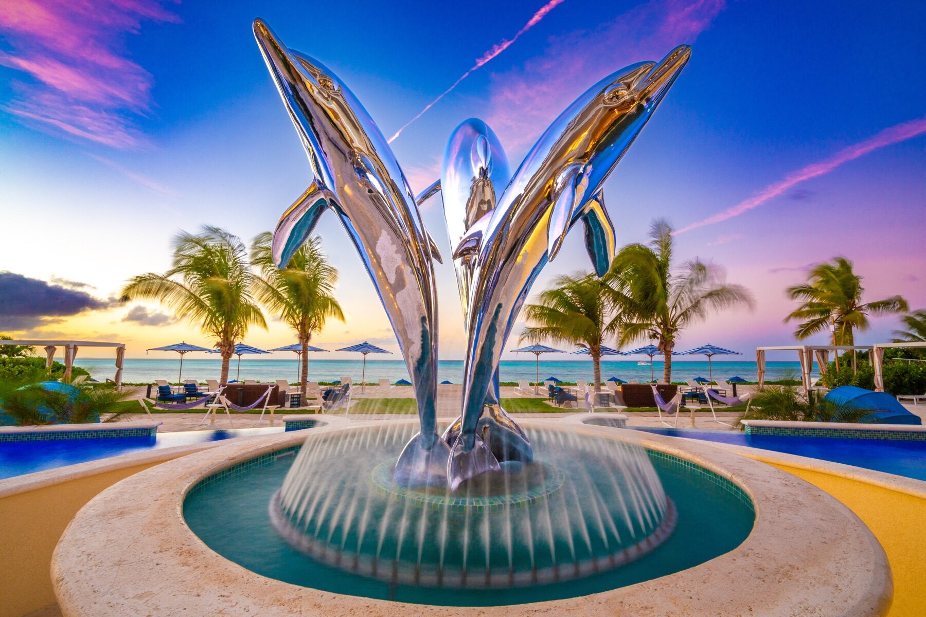 Chrome dolphin fountain sculpture spraying water in a resort courtyard