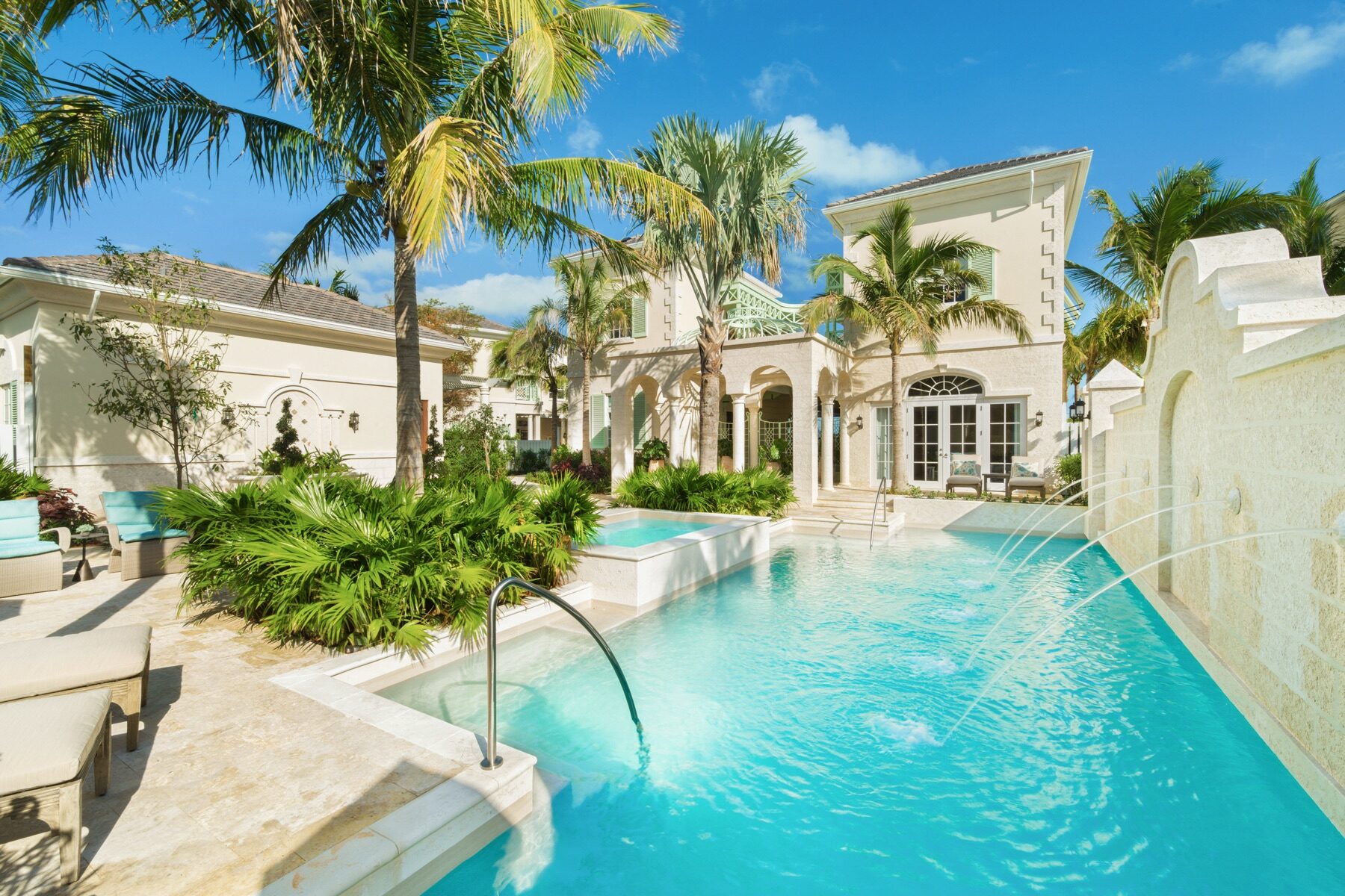 Curving courtyard pool with water jets framed by palm trees and a villa