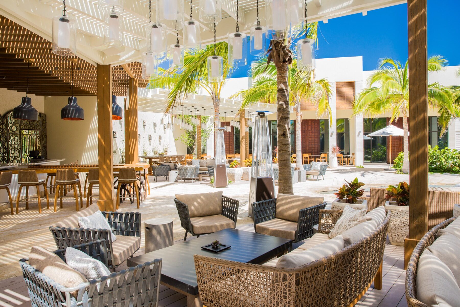 Outdoor lounge with woven rattan chairs and hanging pendant lights near a bar