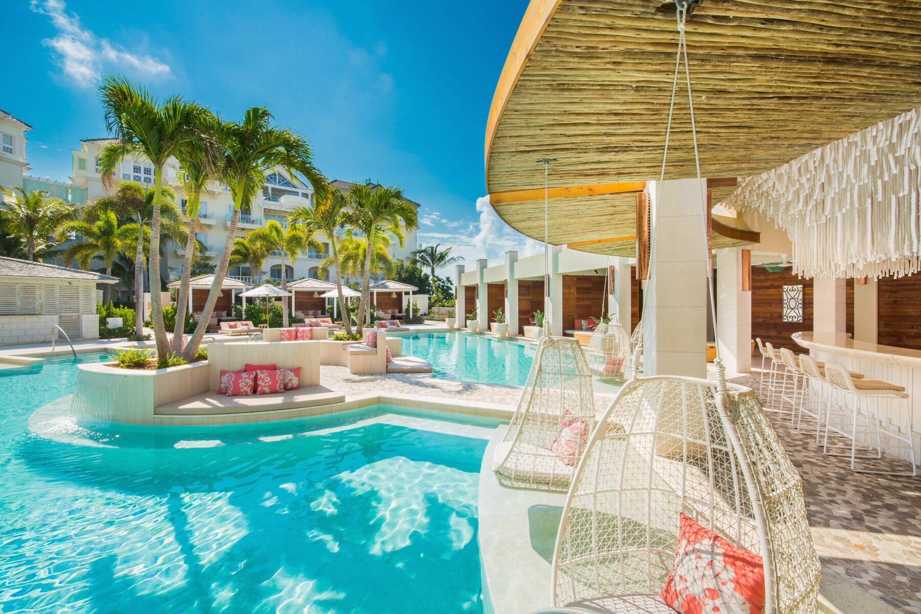 Resort pool with hanging woven chairs beside a thatched roof bar