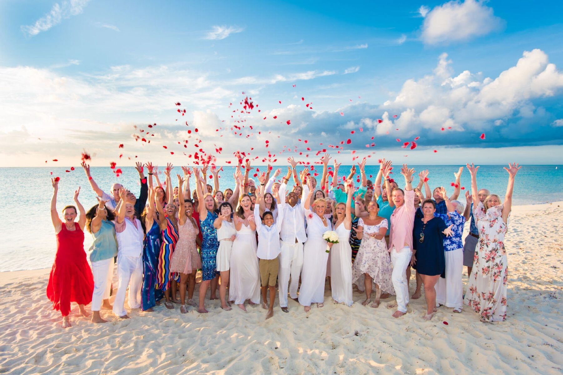 Wedding guests cheering and tossing red rose petals into the air on the sand