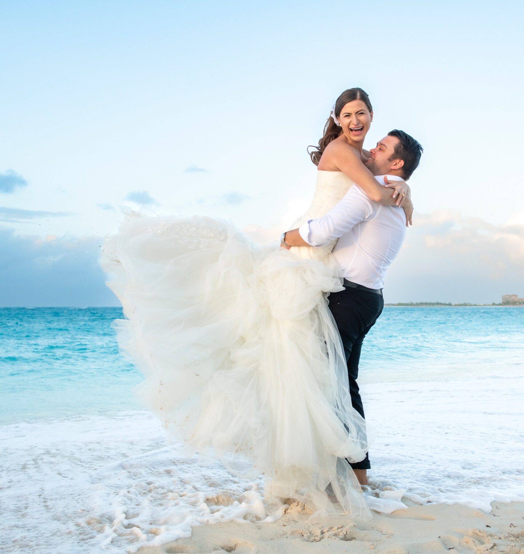 Groom lifting laughing bride as her tulle skirt billows in the Turks and Caicos surf