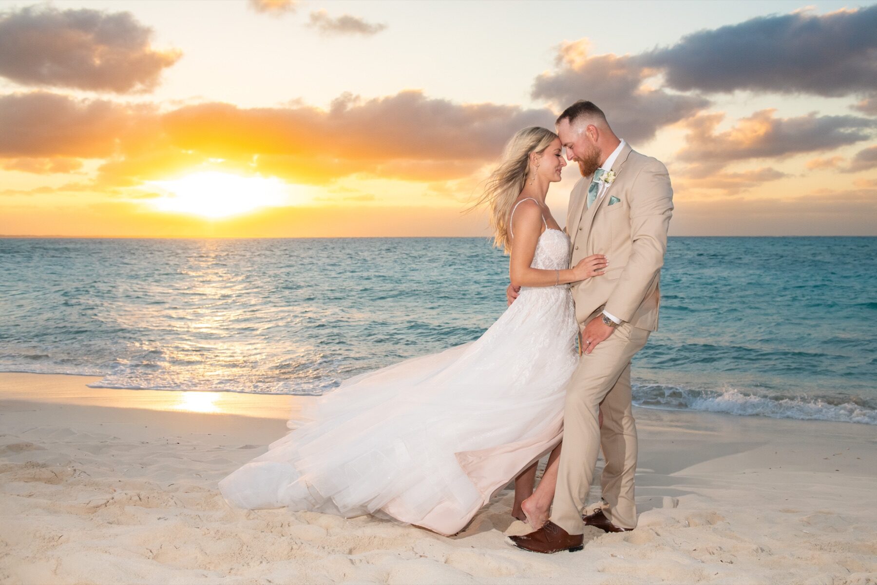 Couple embracing on the beach as the sun sets in orange behind them
