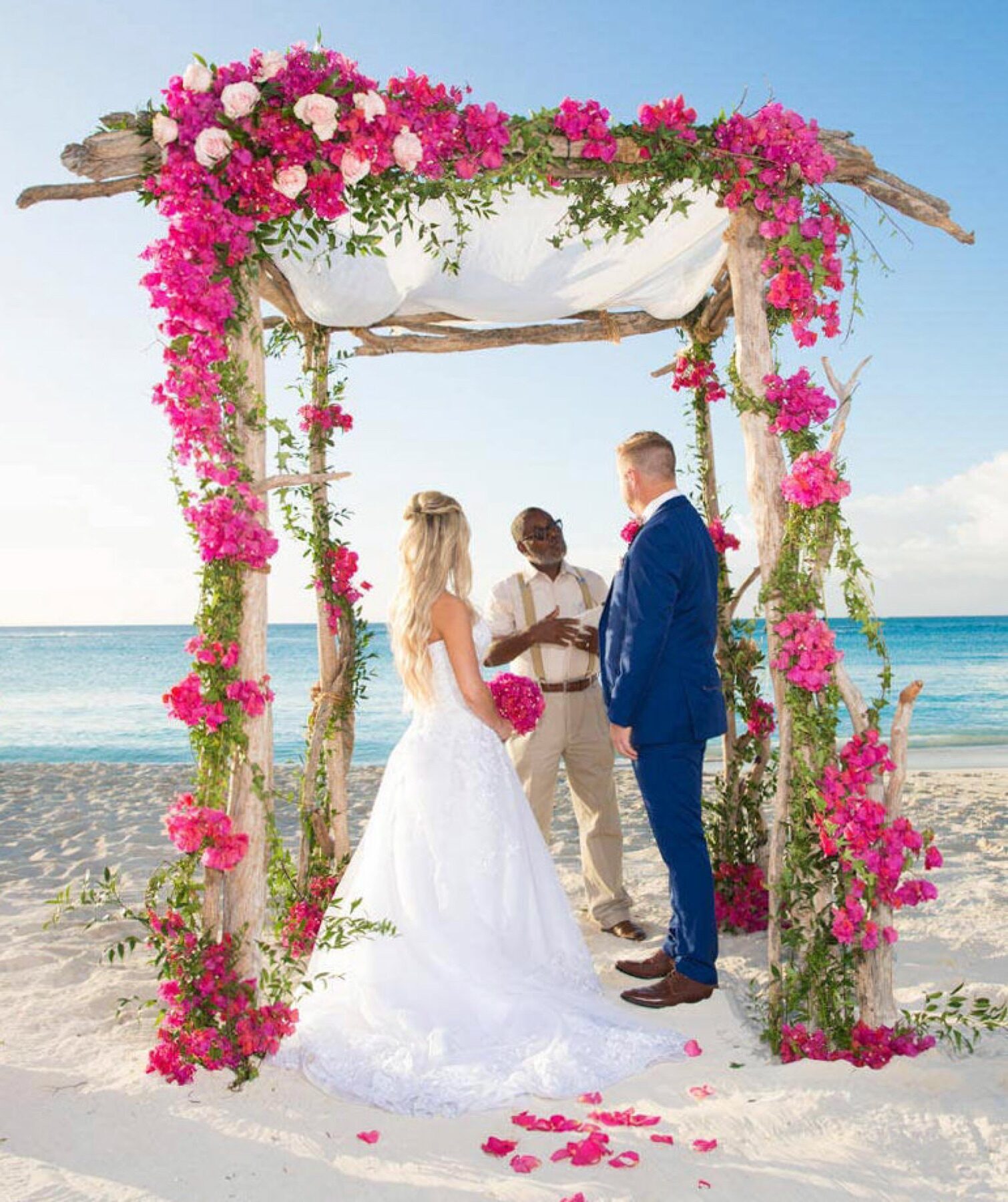 Bride and groom exchanging vows under a bougainvillea covered wooden arbor by the Turks and Caicos shore