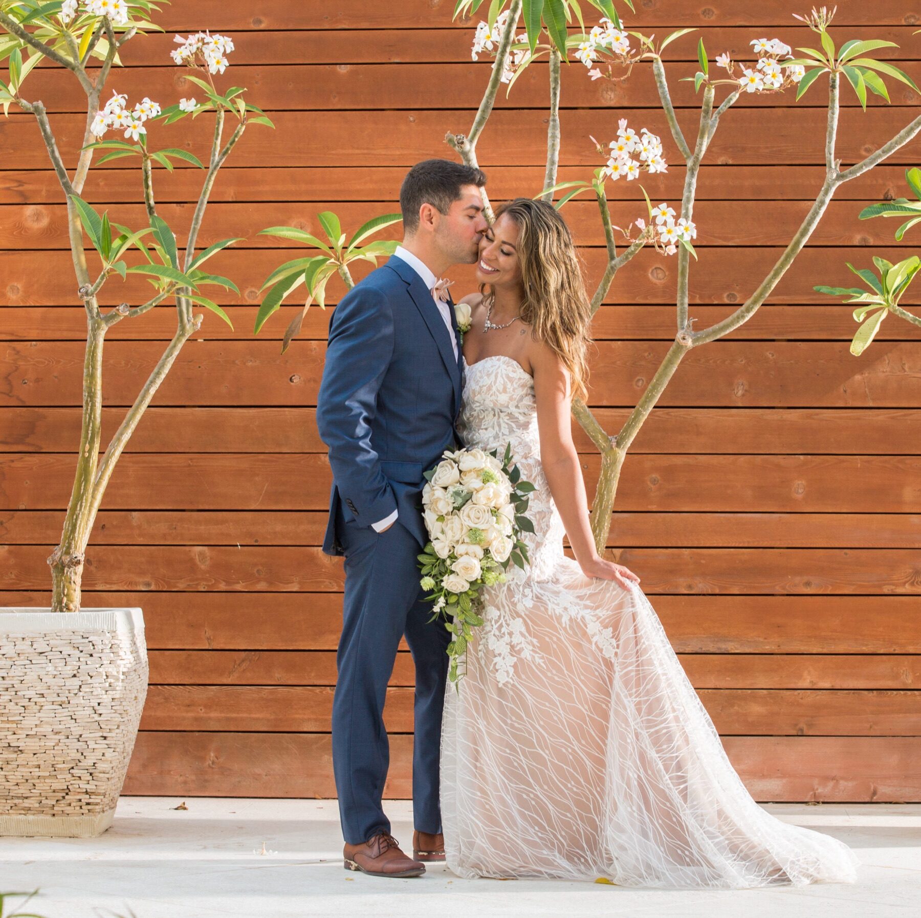 Bride and groom kissing in front of a wooden fence surrounded by flowering trees